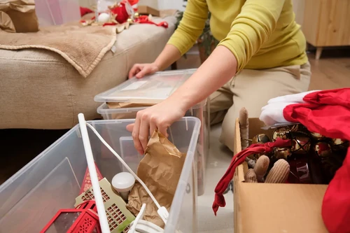 Person placing Christmas decorations into plastic storage bins at home. 